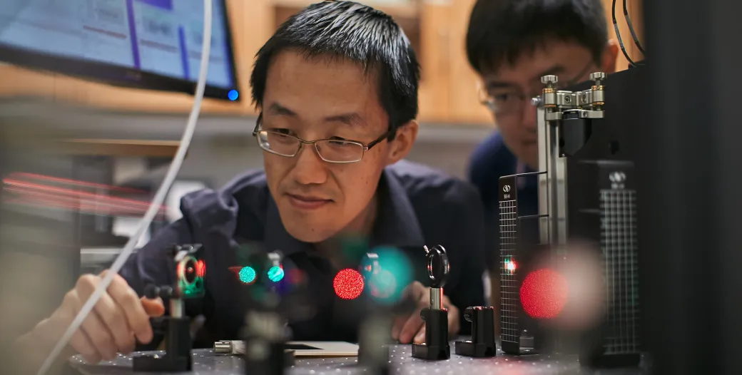 "Matt Lew looks over a field of lasers while a student watches"